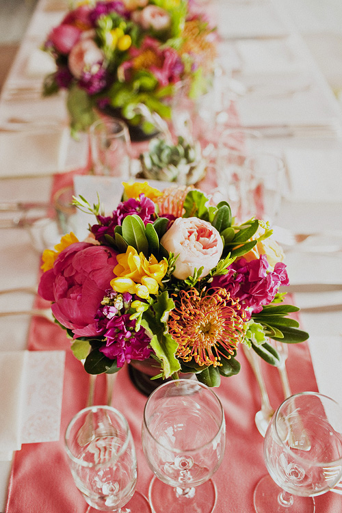 Bright centerpieces and coral runners create a romantic and lively vibe. Hana Floral Design, photo by Sloan Photographers.