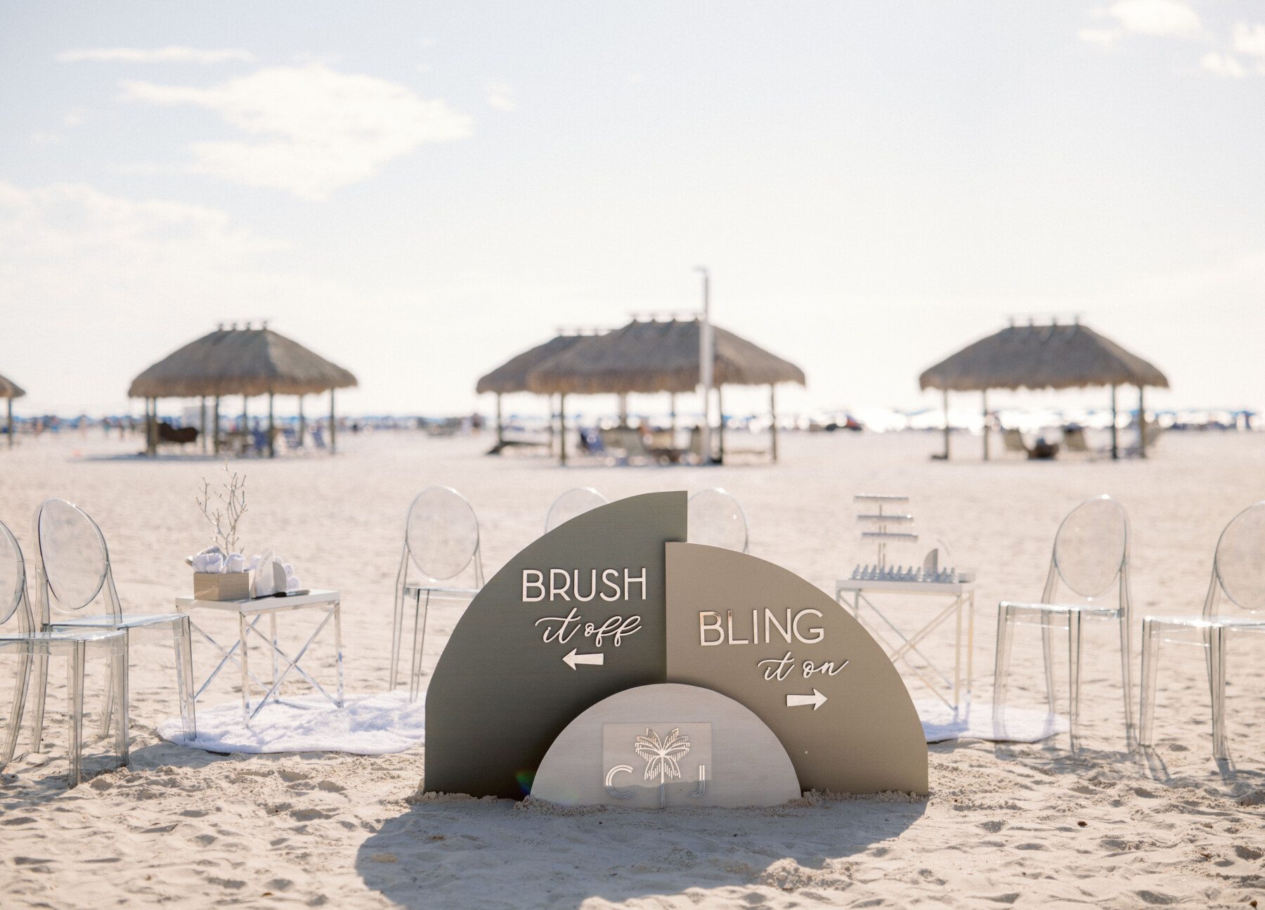 luxe beach wedding set up with signage reading Brush it Off and Bling it On directing guests to stations for decorating their feet for a barefoot wedding