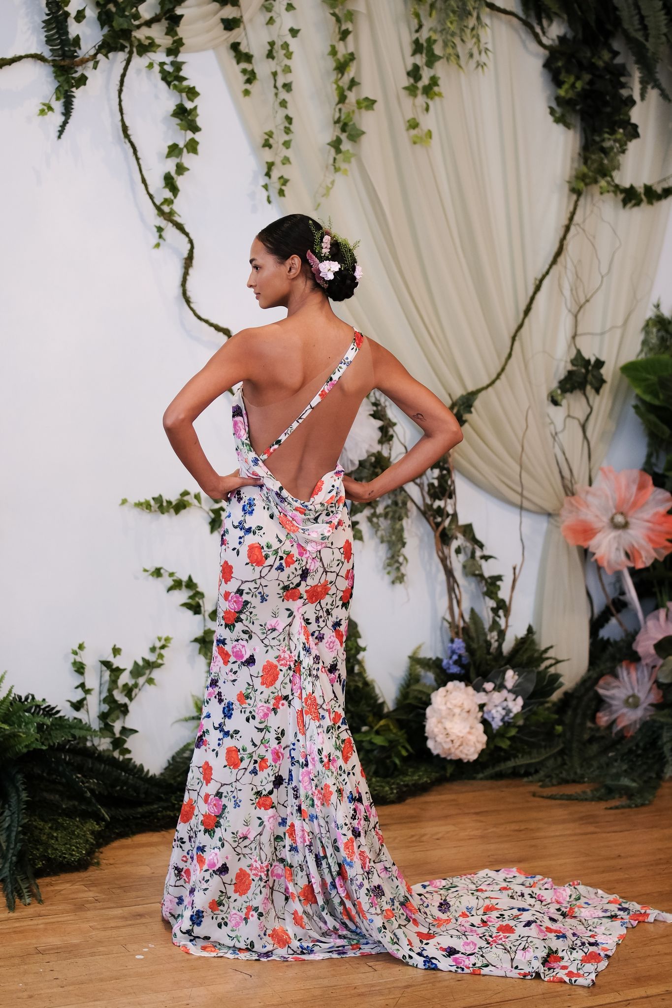 White dress covered with bright, colorful floral pattern. Dress has a statement open back with a singular strap of the same floral print across the back from the right shoulder to left low back. 
